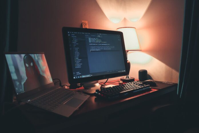 Ciepło oświetlone domowe biuro z dwoma monitorami do programowania Ciepło oświetlone domowe biuro z dwoma monitorami do programowania