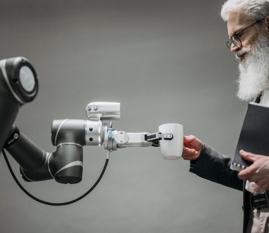 Starszy mężczyzna odbiera kubek od ramienia robota w nowoczesnym biurze