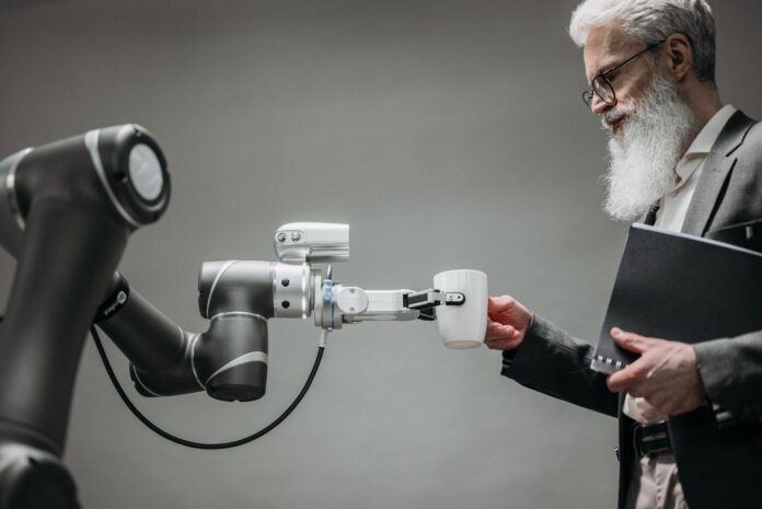 Starszy mężczyzna odbiera kubek od ramienia robota w nowoczesnym biurze